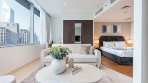 A modern hotel room with a large window, a sofa, a bed, and a coffee table with a vase of flowers. - StayShort - Sky Gardens Studio with Skyscraper Views in DIFC! (DIFC)