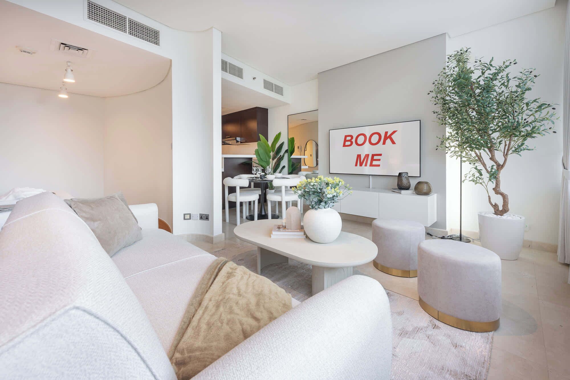 Ein modernes Wohnzimmer mit einer Couch, Poufs, einem Couchtisch und einem Essbereich im Hintergrund.