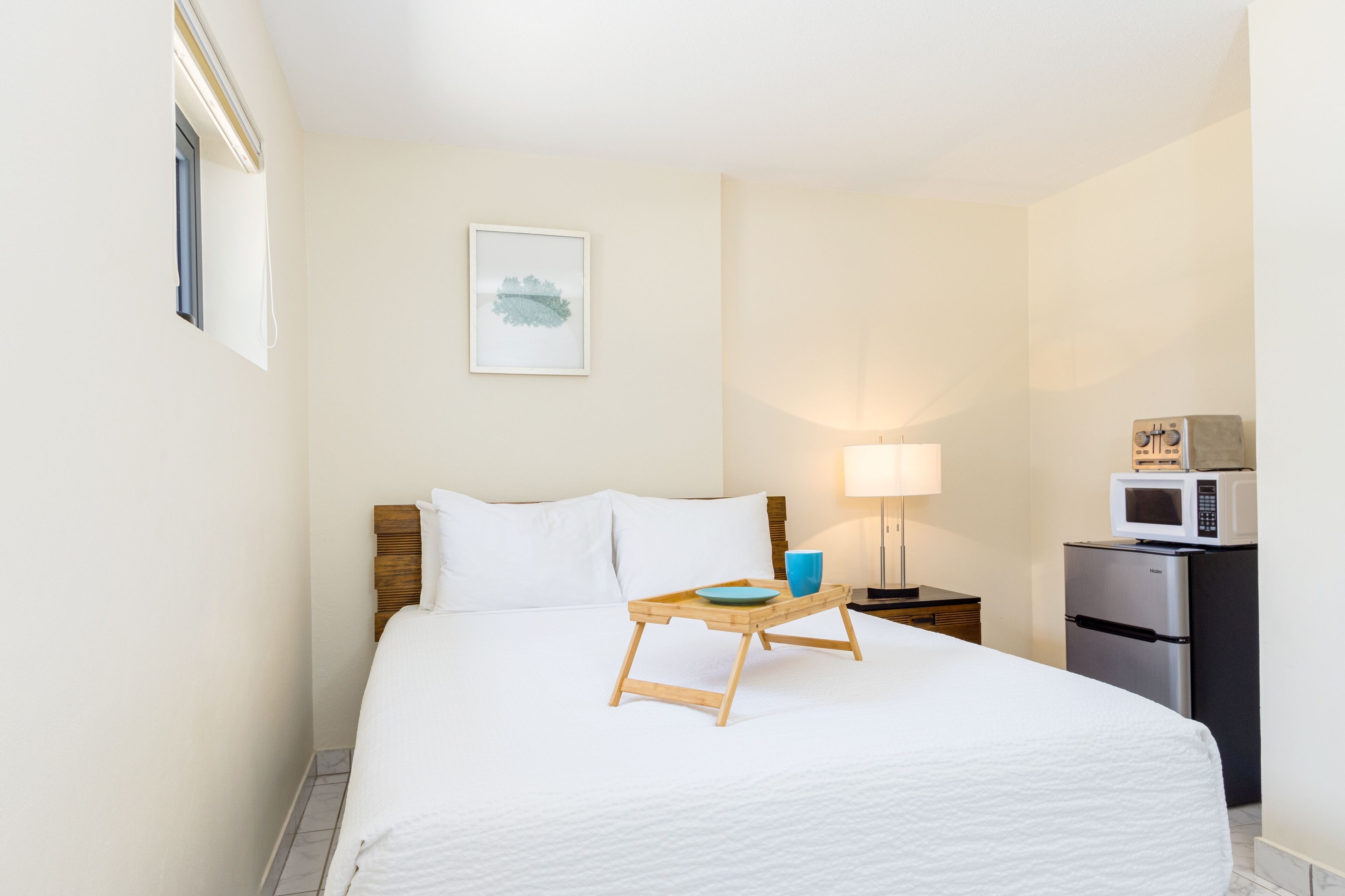 A hotel room with a bed, a bedside table with a lamp, a microwave, and a refrigerator.