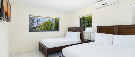 Ett hotellrum med två sängar, ett stort fönster med utsikt över palmer och en luftkonditioneringsanläggning på väggen.