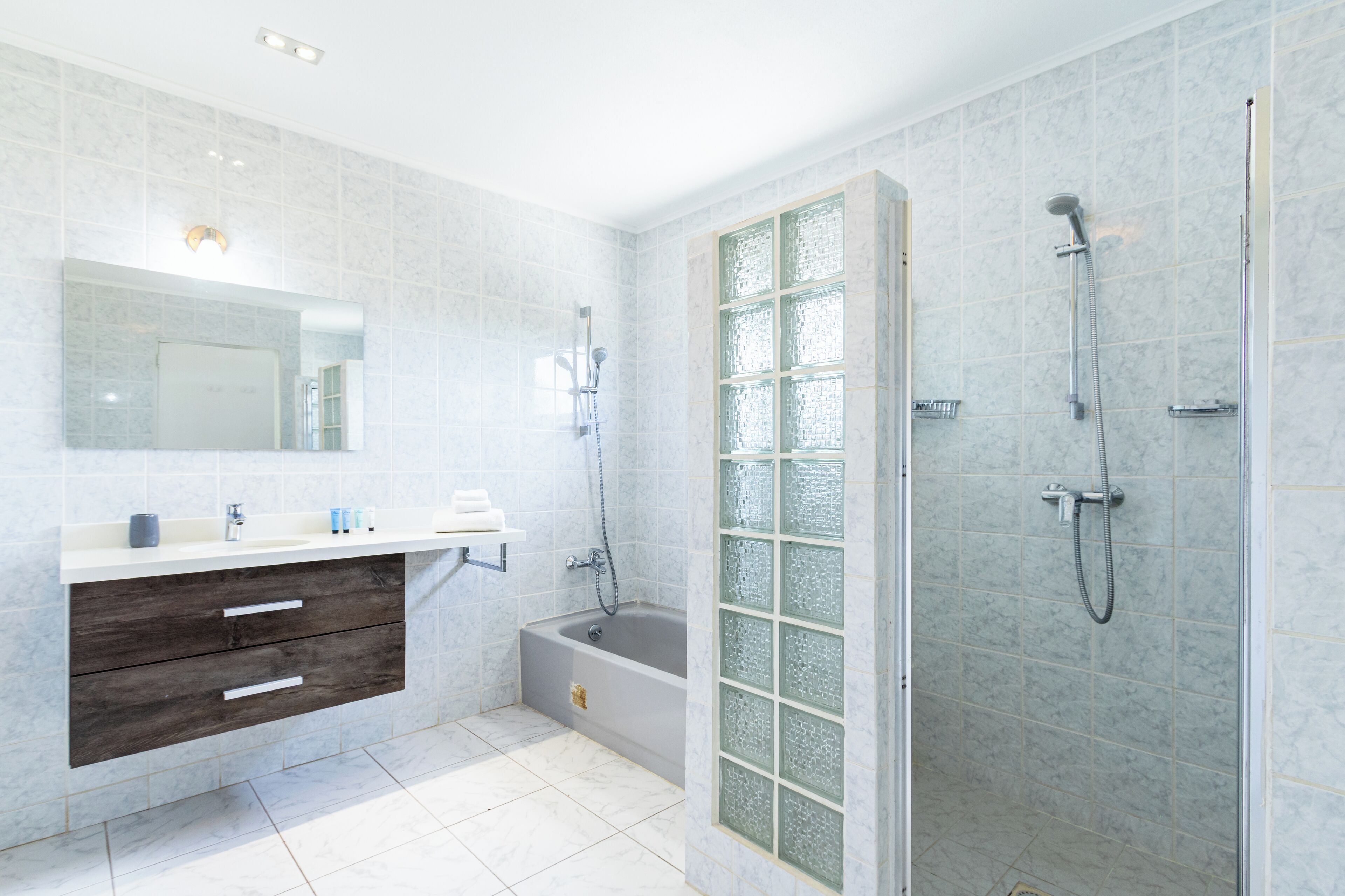 A modern bathroom with a large mirror, a vanity with drawers, a bathtub, and a shower area.