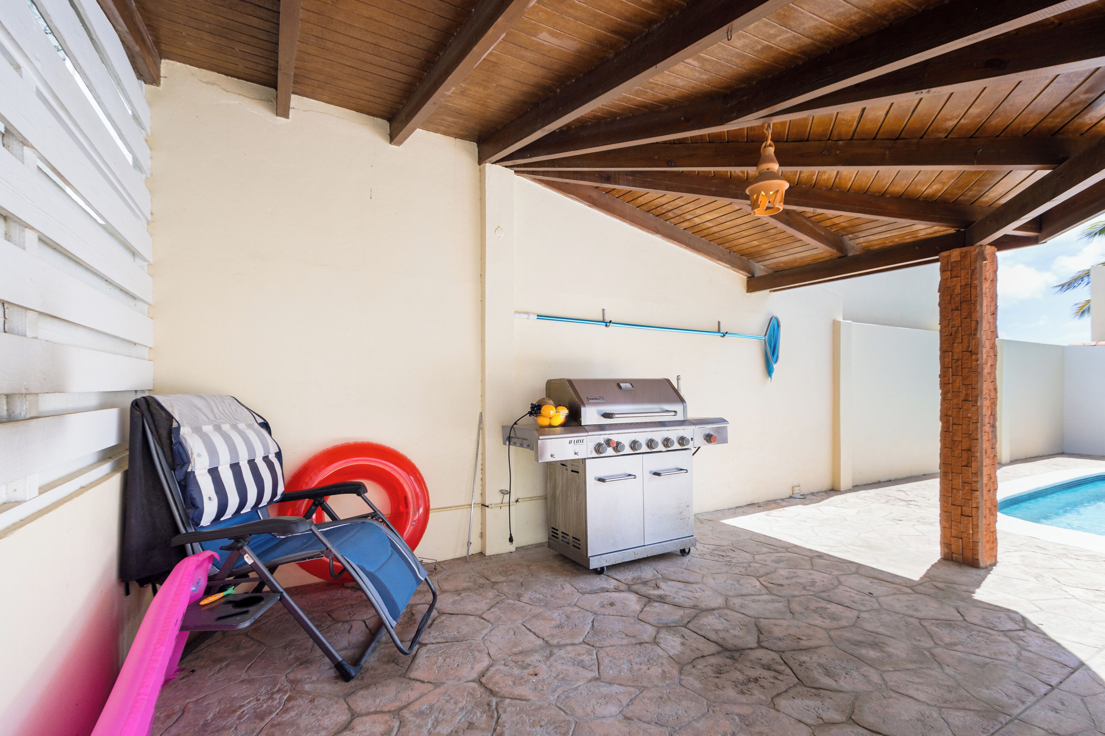 Une terrasse extérieure avec un barbecue, une chaise pliante et une piscine en arrière-plan.