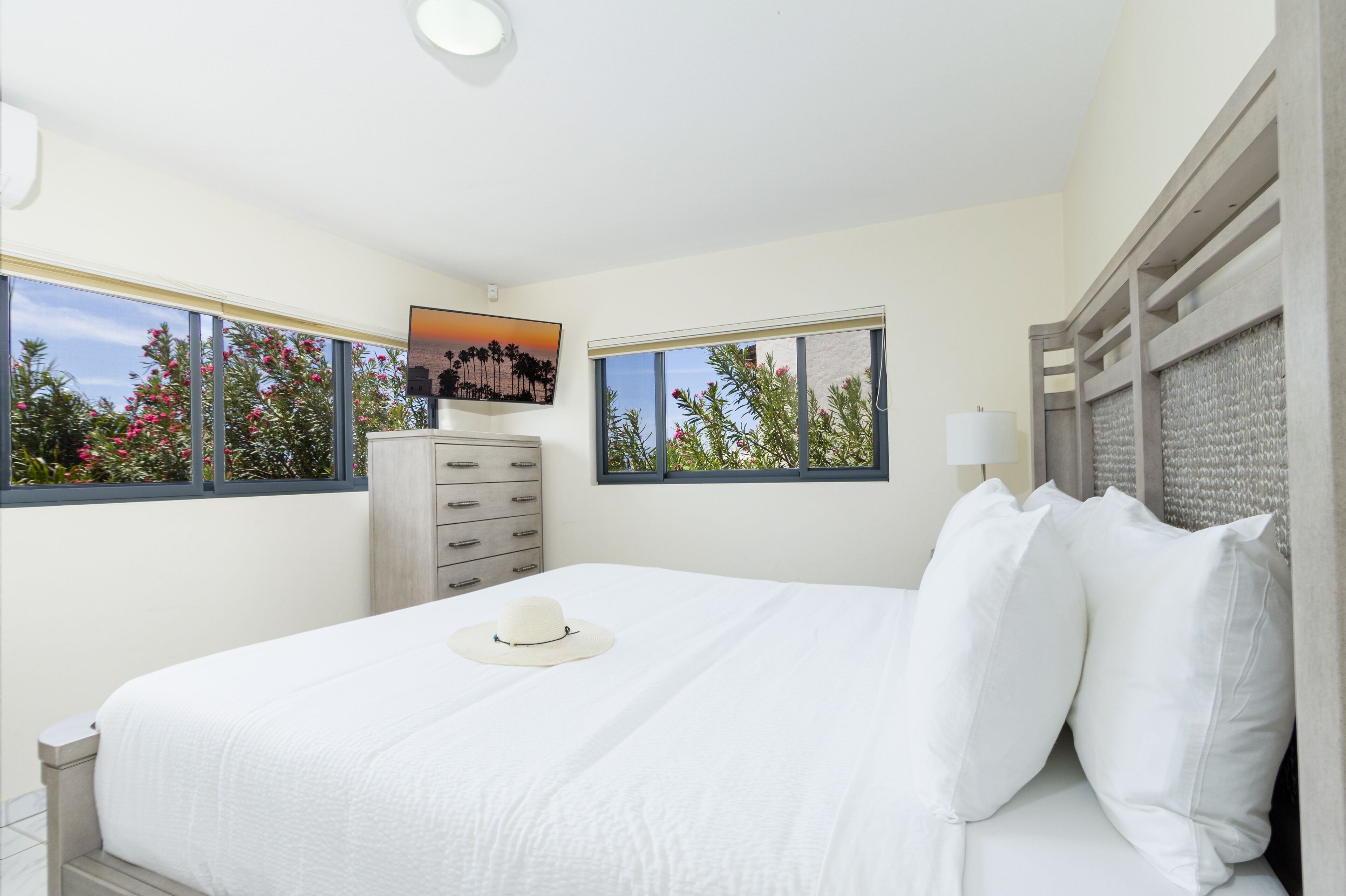 Une chambre à coucher avec un lit, une commode, une table de chevet et deux fenêtres.