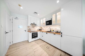 A modern kitchen with white cabinetry, a built-in oven, a microwave, and a wooden countertop.