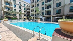 A swimming pool with lounge chairs and palm trees, surrounded by a multi-story building with balconies. - Free housekeeping visits during your stay - StayShort - Spectacular 1-Bedroom perfect for 4 in The Greens (Dubai)