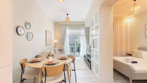 Una sala de estar moderna con un sofá, un comedor con una mesa dispuesta para cuatro personas y un gran ventanal con cortinas.