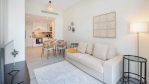 Una sala de estar moderna con un sofá blanco, un comedor con mesa y sillas, una cocina al fondo y una lámpara de pie.