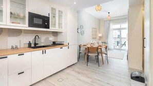 Una cocina moderna con armarios blancos, un microondas negro y una encimera de madera. Hay una zona de comedor con una mesa y sillas.