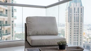 Varanda com cadeira estofada e pequena mesa com planta, com vista para paisagem urbana com edifícios modernos.
