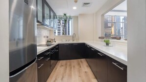 Cozinha moderna com armários pretos, uma geladeira de aço inoxidável e uma janela com vista para edifícios.