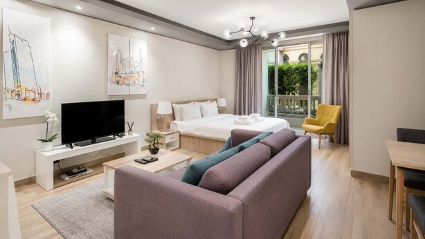 Une chambre d’hôtel moderne équipée d’un lit, d’une télévision, d’un canapé, d’une table à manger et d’un balcon avec des rideaux.