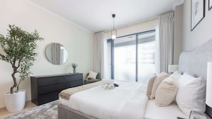Un dormitorio moderno con una cama grande, una mesita de noche, un aparador, una planta en maceta y una ventana con cortinas.