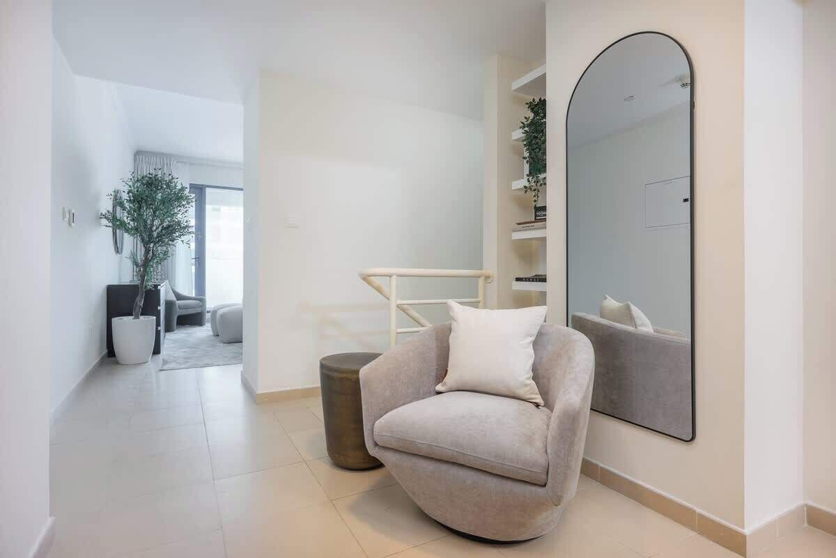 Een moderne woonkamer met een grijze fauteuil, een grote spiegel en een potplant.