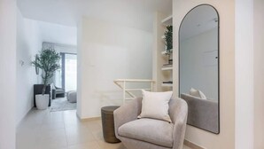 Una sala moderna con un sillón gris, un espejo grande y una planta en maceta.