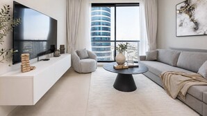 Una sala de estar moderna con un televisor de pantalla plana, una mesa de centro redonda, un sofá gris y un mueble de entretenimiento blanco.