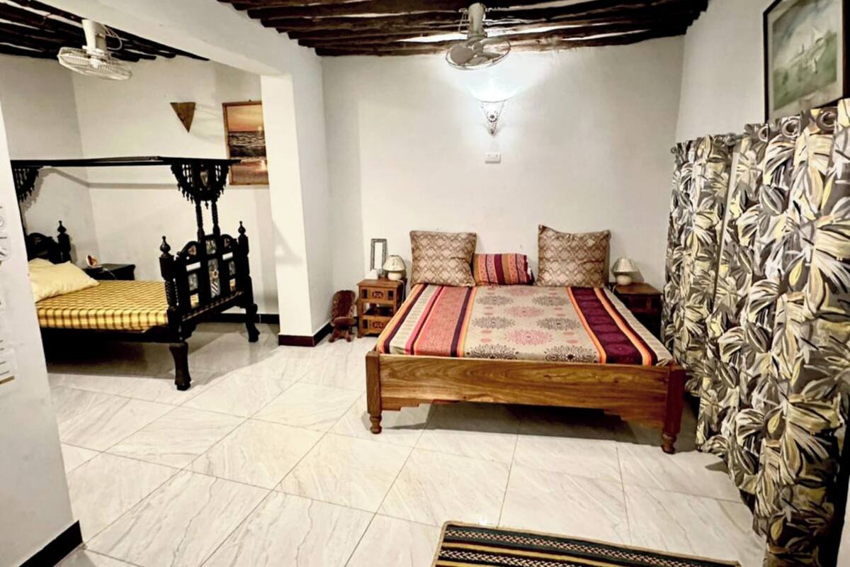 Une chambre à coucher avec un grand lit, un lit plus petit, une table de chevet, une lampe et un ventilateur de plafond.