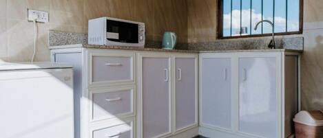 Una cocina compacta con microondas, hervidor y ventana sobre el fregadero.