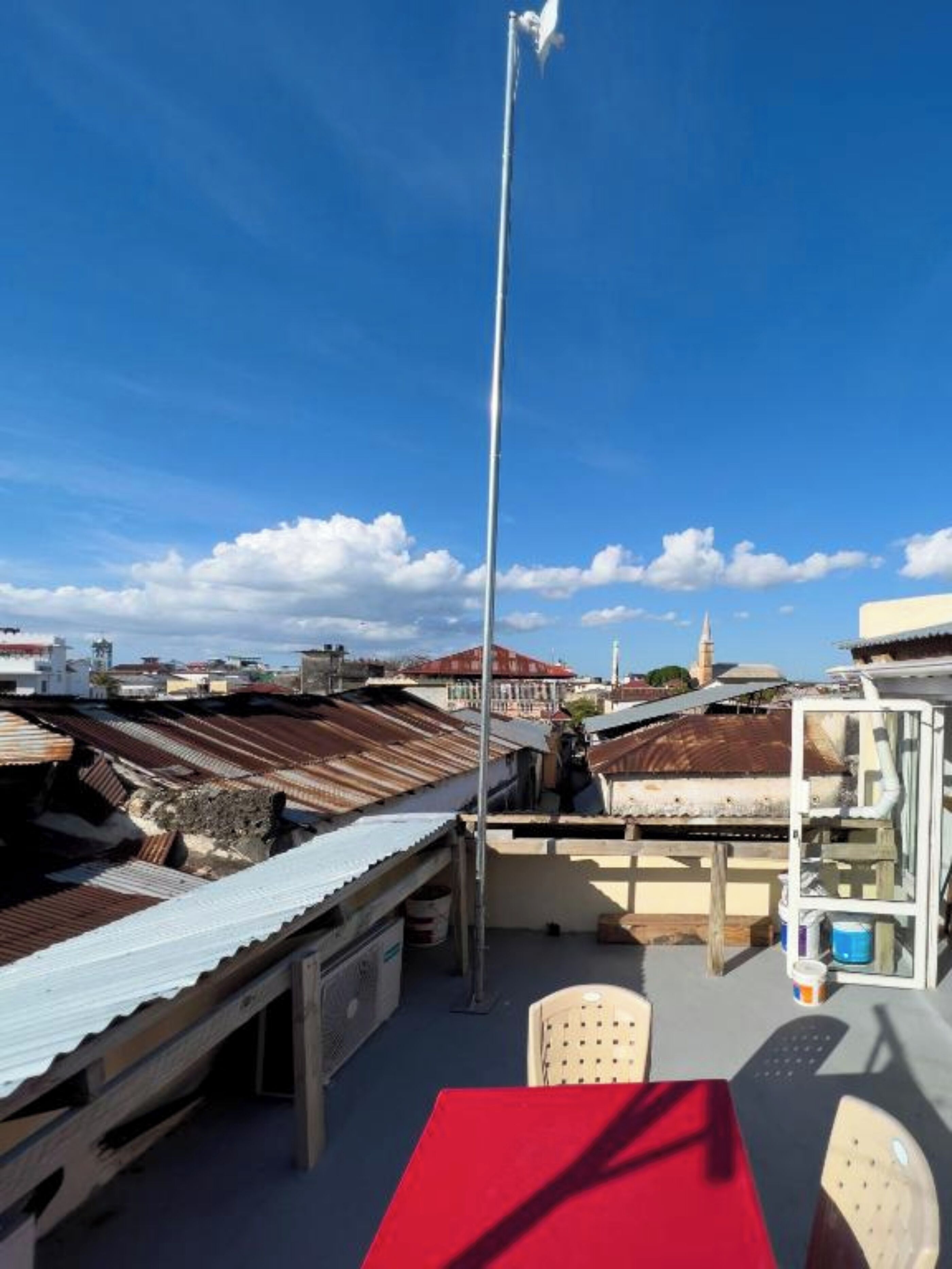 Une terrasse sur le toit, avec une table et des chaises rouges, un poteau en métal et une vue sur les bâtiments environnants.