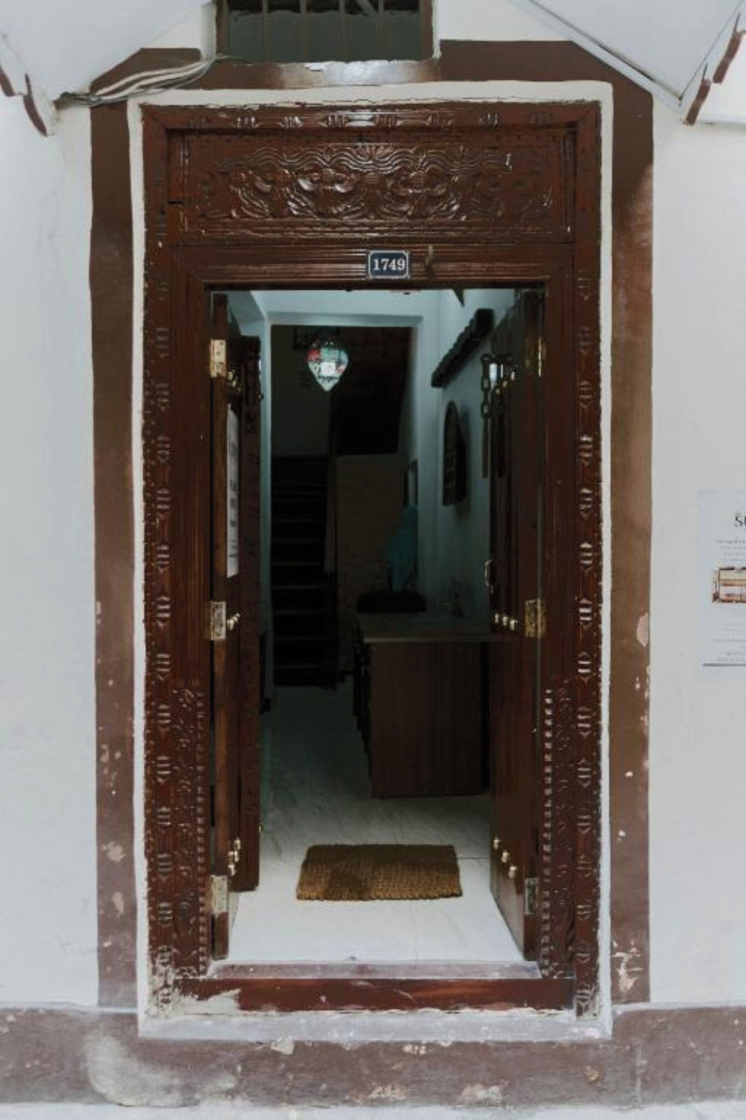 A wooden door with a number plate, leading into a hallway with a staircase and a small table.