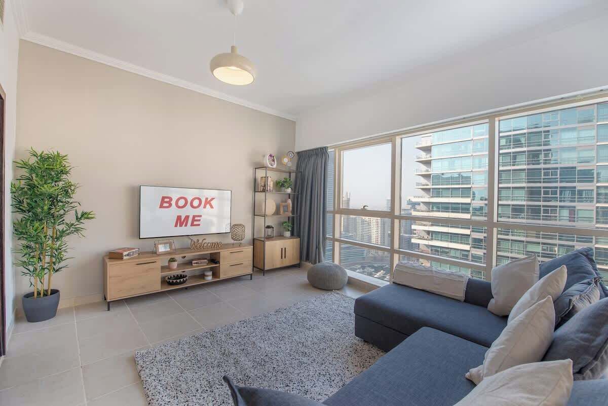 A modern living room with a large window, a sofa, a TV, and a bookshelf.