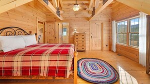 A wooden cabin bedroom with a bed, a colorful rug, a dresser, and a window. - Remmert`s Log Haven - Tranquil Mountain Getaway (Estes Park)