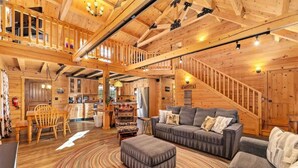 A spacious wooden cabin interior with a living area featuring a gray sofa, ottoman, and a patterned rug. - Remmert`s Log Haven - Tranquil Mountain Getaway (Estes Park)