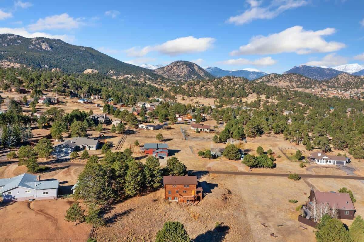 An aerial view of a residential area with houses, roads, and mountains in the background.