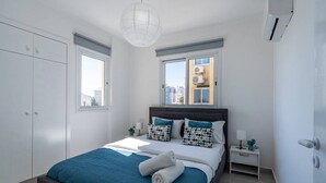 A bedroom with a bed, bedside tables, a wardrobe, and a window. - Andrea 3-Bedroom Apt in Mackenzie W/ Pool (Cyprus - Larnaca)