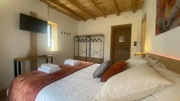 A bedroom with a wooden ceiling, a bed with white and brown bedding, a TV mounted on the wall, and a coat rack with hangers.