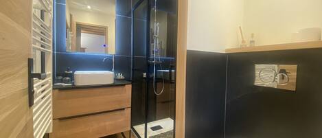Un baño moderno con cabina de ducha de vidrio, un lavabo blanco y un mueble de tocador de madera.