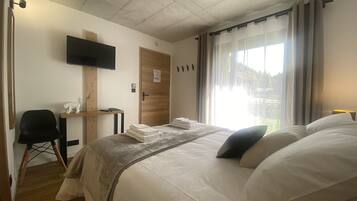 A hotel room with a bed, a desk, a chair, a TV mounted on the wall, and a window with curtains.