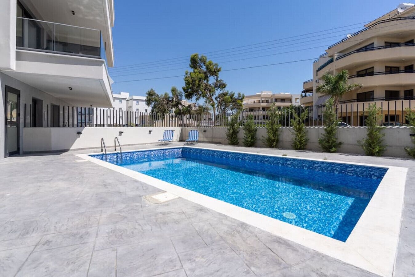 Una piscina rettangolare con bordo piastrellato, circondata da un piccolo muro e alberi.