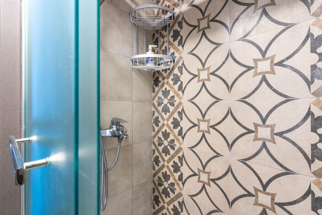 A shower area with a glass door and a tiled wall featuring a geometric pattern.