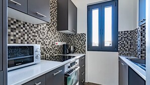 A compact kitchen with a microwave, oven, and coffee maker, featuring checkered tile backsplash and a window. - Maryam's 2-BR Apt Facing Larnaca Harbor W/ Pool (Cyprus - Larnaca)