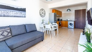A modern apartment with a grey sofa, a dining table, and a kitchen area including a washing machine.