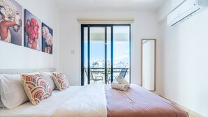 A bedroom with a bed, pillows, a balcony with a view, and a large window.