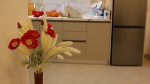 A modern kitchen with a stainless steel refrigerator, beige cabinets, and a vase with red and white flowers on a table. - Vila Murati (Ksamil)