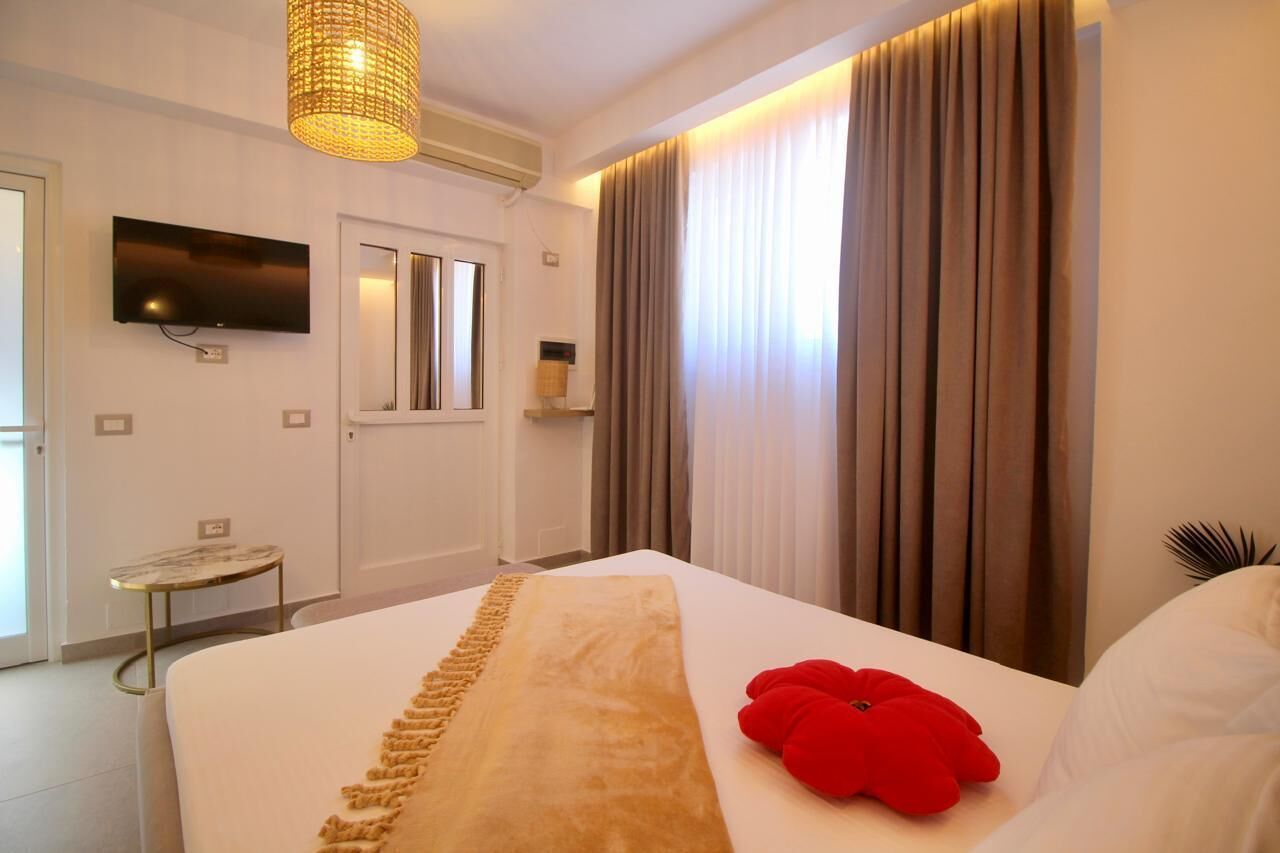 A hotel room with a large bed, a television mounted on the wall, a small table, and a window with curtains.