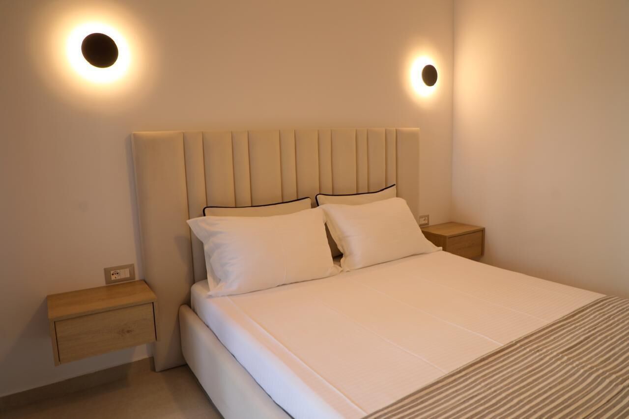 A bedroom with a bed, two bedside tables, and wall-mounted lights.