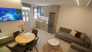 A modern living room with a grey sofa, a round dining table with chairs, and a TV mounted on the wall. - Vila Murati (Ksamil)