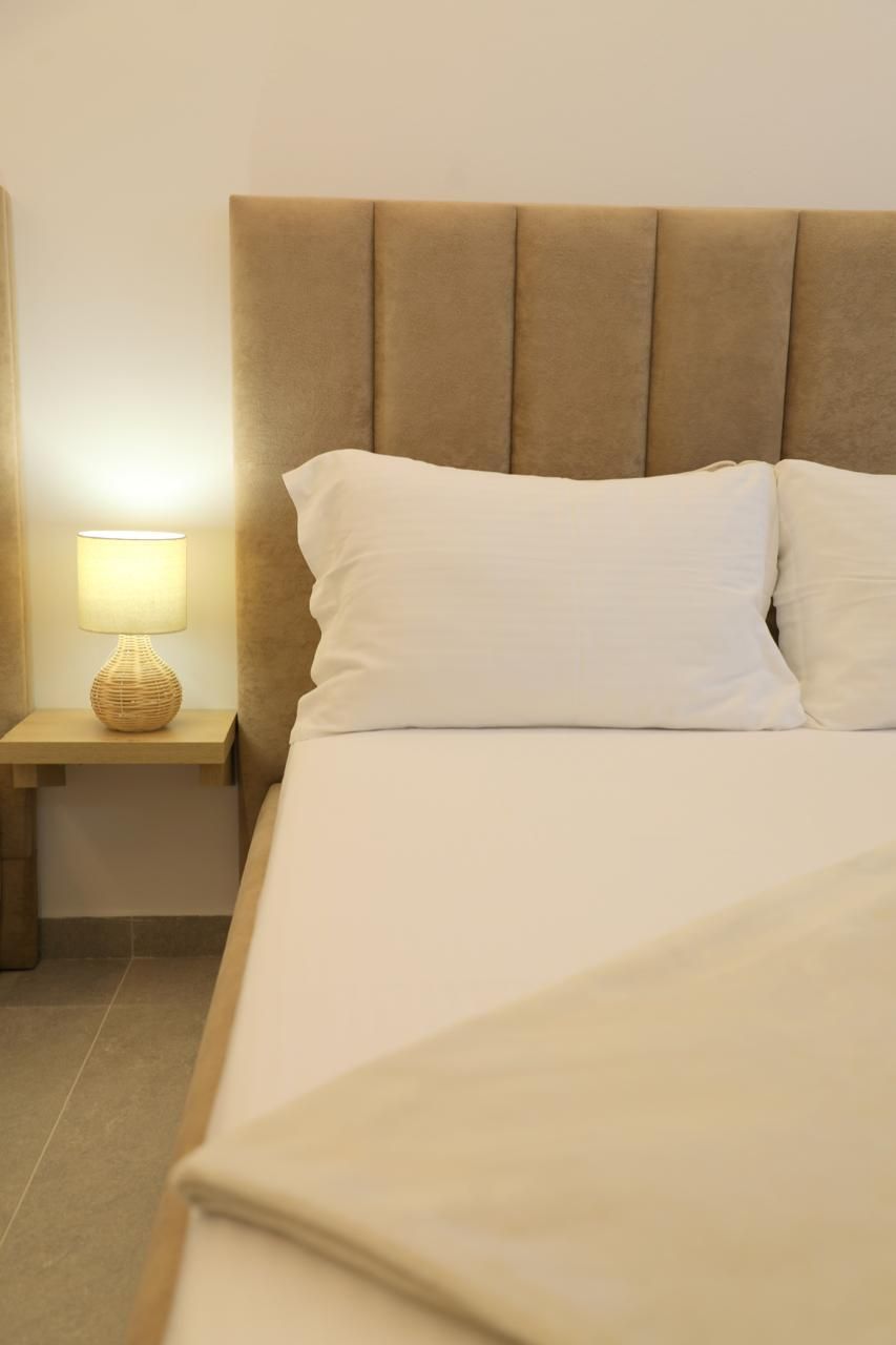 Una cama bien hecha con cabecera, lámpara de noche y mesita de noche.