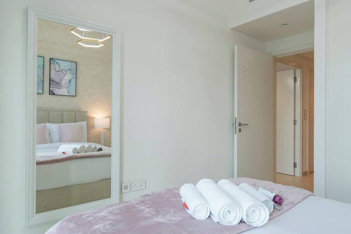 Een hotelkamer met een bed, een spiegel, een wandlamp en een deur naar een andere kamer.