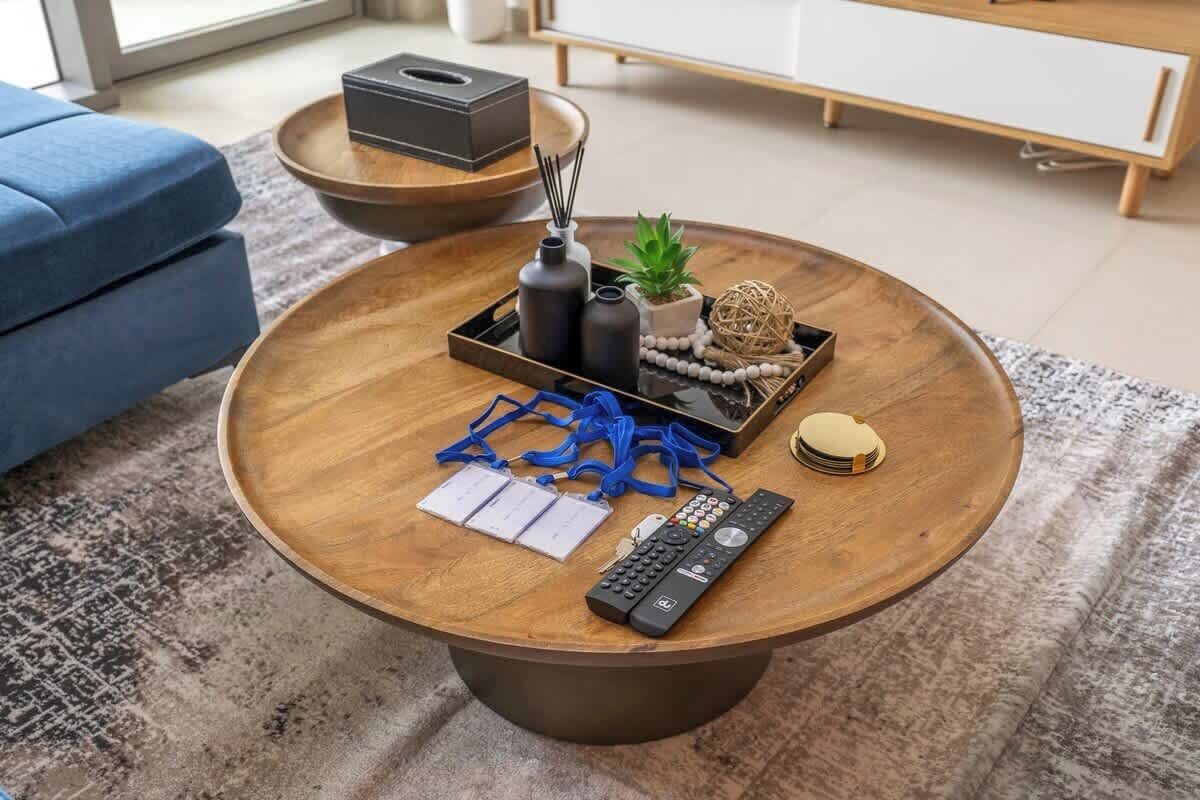 Ein runder Couchtisch aus Holz mit einer Fernbedienung, Papier und Dekorationselementen.