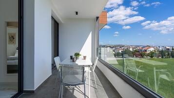 A balcony with a table and chairs, a potted plant, and a view of a green landscape and buildings.