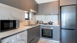 Eine moderne Küche mit grauen Schränken, einem Edelstahlkühlschrank, einer Mikrowelle, einer Waschmaschine und einem Backofen.