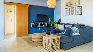 A living room with a grey sofa, a TV, and a wall-mounted shelf with plants. - Bayview 2-BR Apartment in Larnaca (Cyprus - Larnaca)
