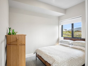 Een slaapkamer met een bed, een houten garderobe en een raam met uitzicht op het omliggende landschap.