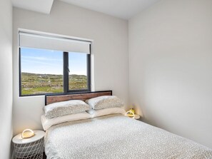 A bedroom with a bed, a nightstand, a lamp, and a window with a view of a landscape.