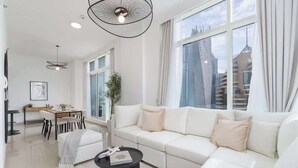 Una sala de estar moderna con un sofá blanco, una mesa de centro negra y un comedor con una mesa y sillas blancas.