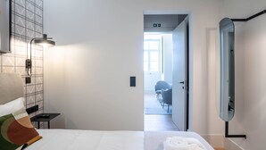 Een hotelkamer met een bed, nachtkastje, lamp, spiegel en uitzicht op de gang en een andere kamer.
